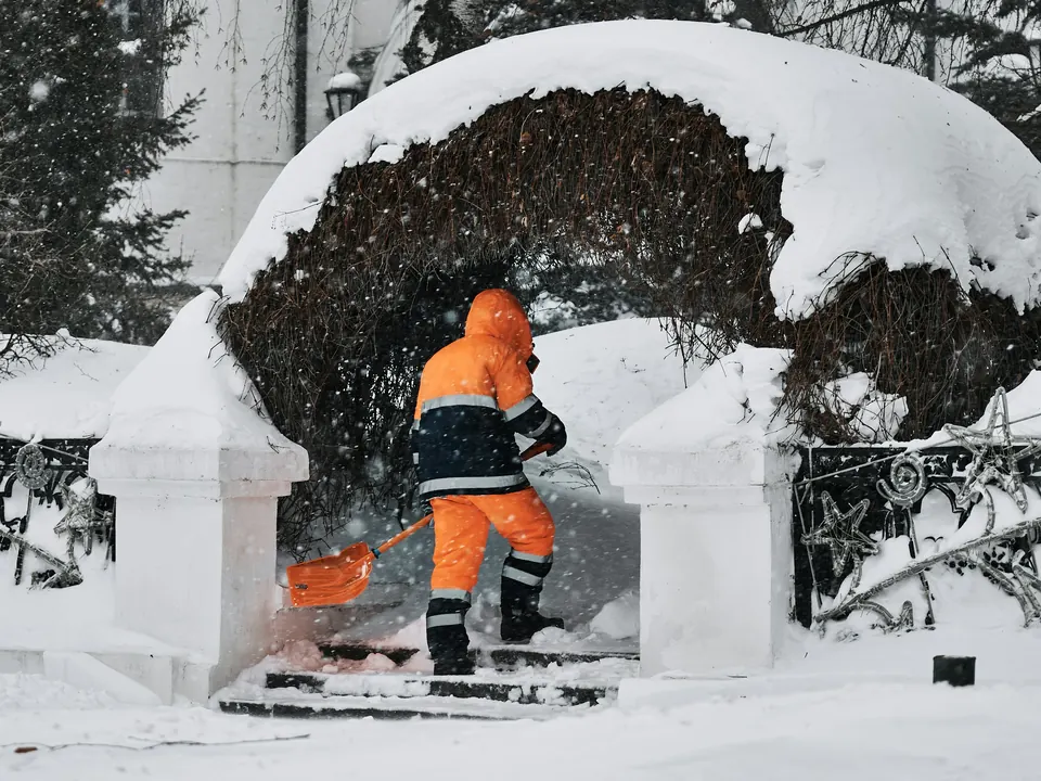 A worker in winter safety gear shovelling snow from front steps